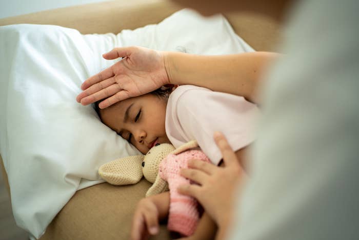 Child sleeping successful  bed, holding a stuffed toy. An big  manus  mildly  checks the child's forehead