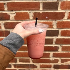 Someone holding up an iced drink in a plastic to-go cup against a brick wall