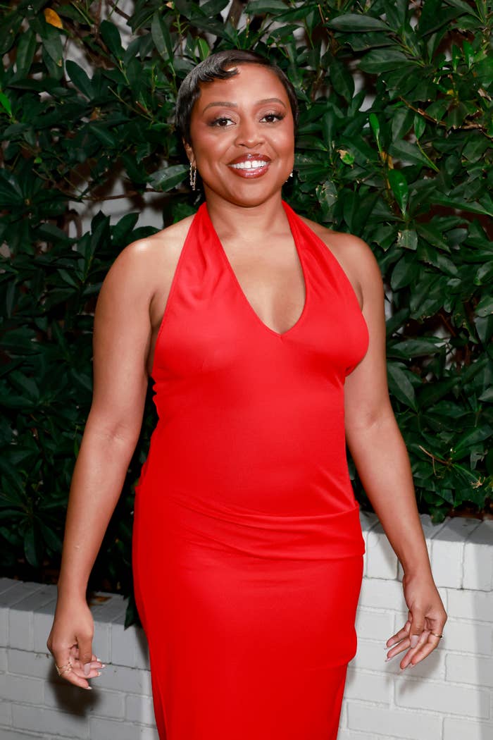 Quinta Brunson successful  a reddish  halter formal  stands smiling against a leafy backdrop