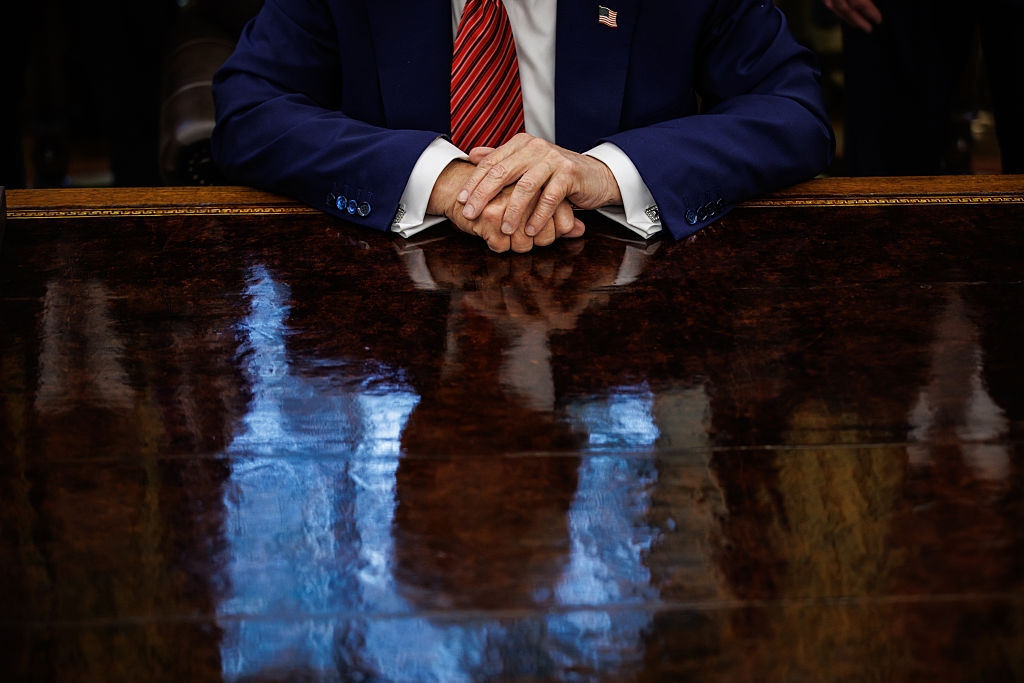 Person i dress med kryssede hender på en reflekterende trebordflate