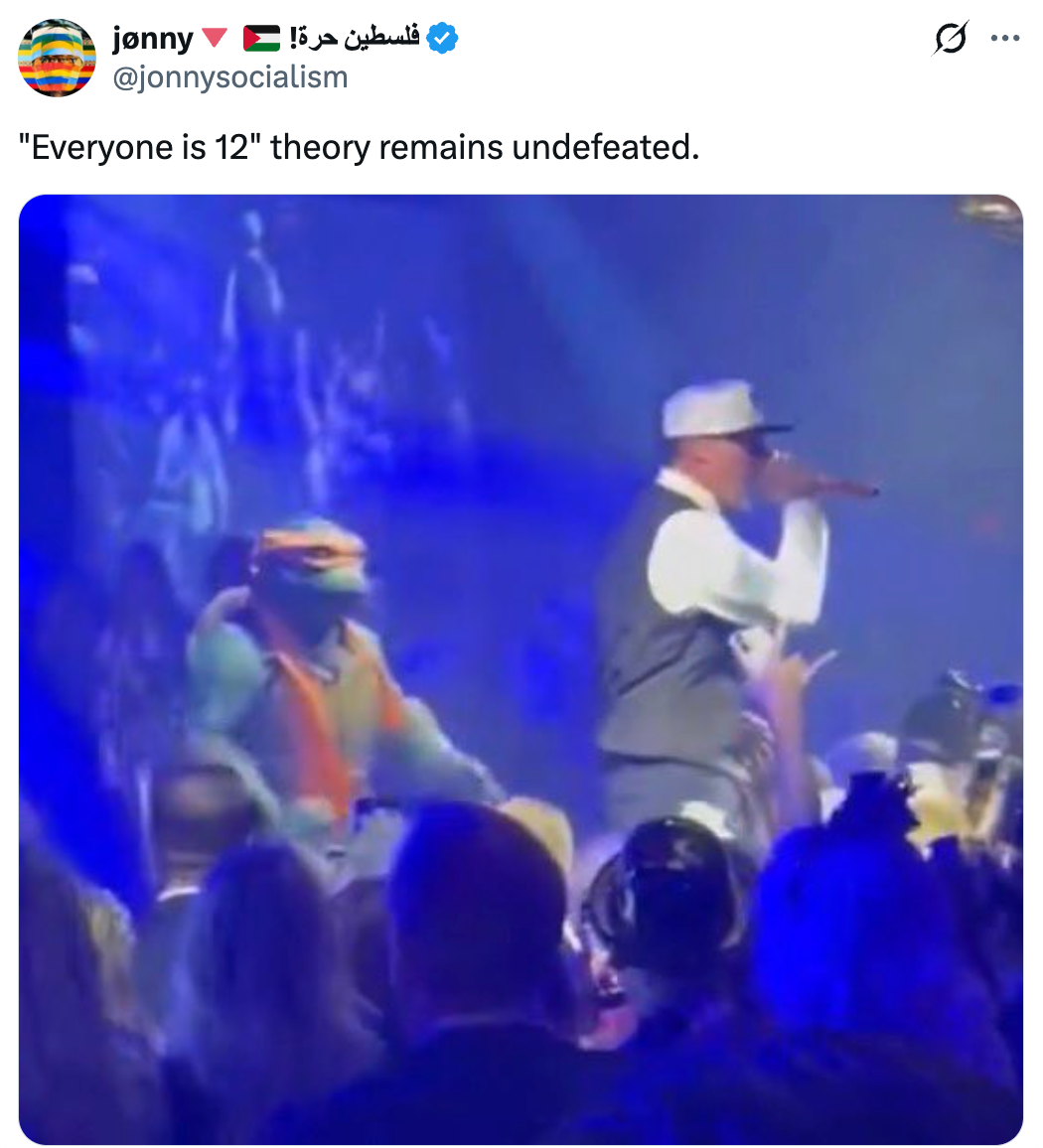 Utøver på scenen med Teenage Mutant Ninja Turtle-karakter, som ser på publikum. Bildeteksten lyder: "'Alle er 12' teorien forblir ubeseiret."
