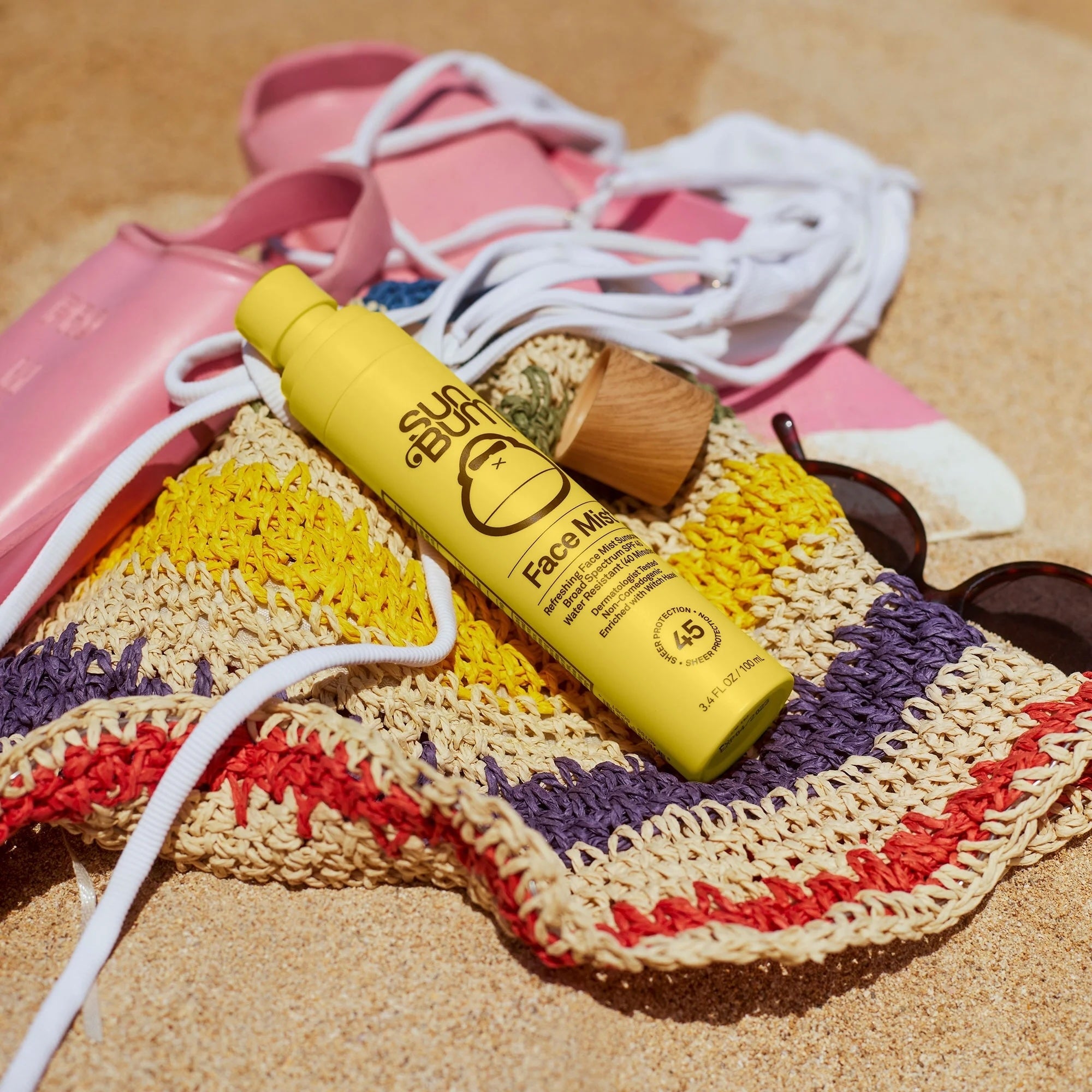 Sunscreen vessel  connected  a woven formation  container  with sunglasses and sandals beside it connected  sand, suggesting indispensable  formation  gear