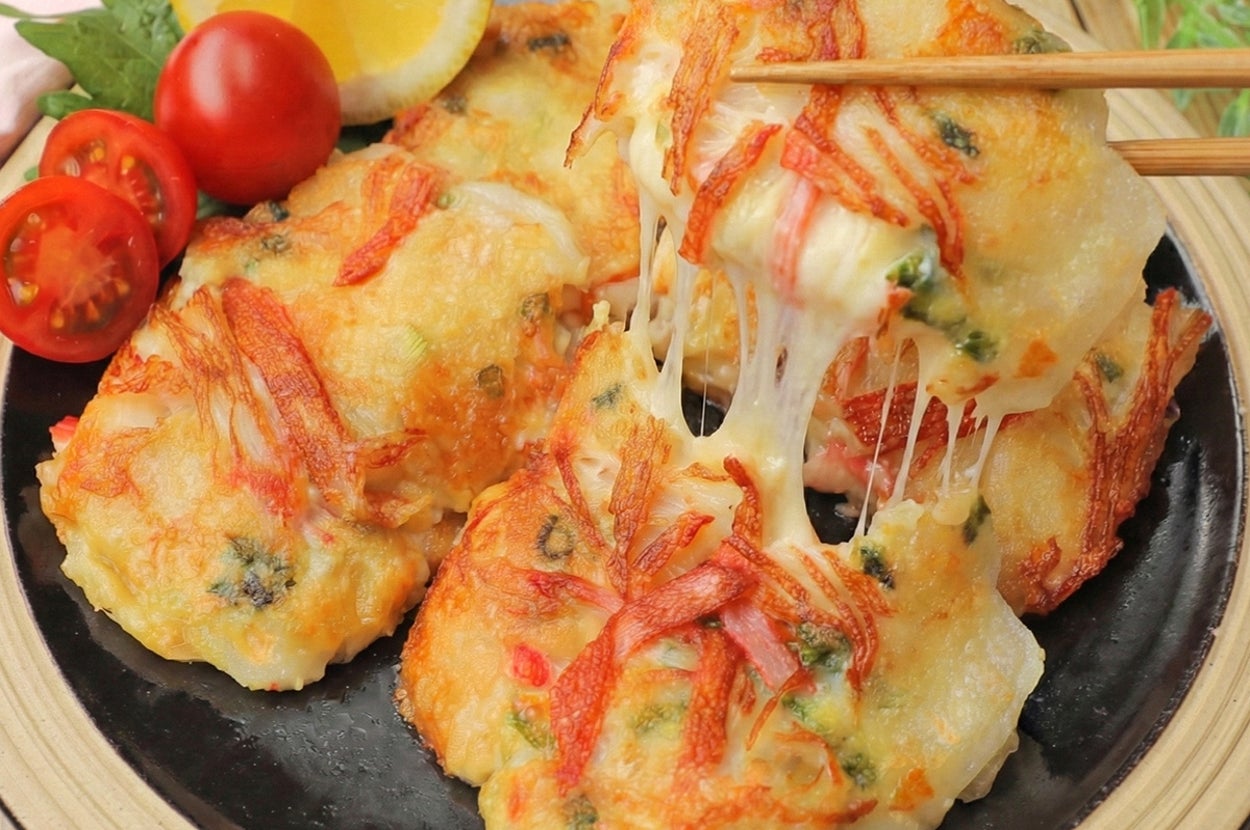 お皿にのった具材入りのチーズがとろけるチヂミ。レモンとトマトが添えられている。