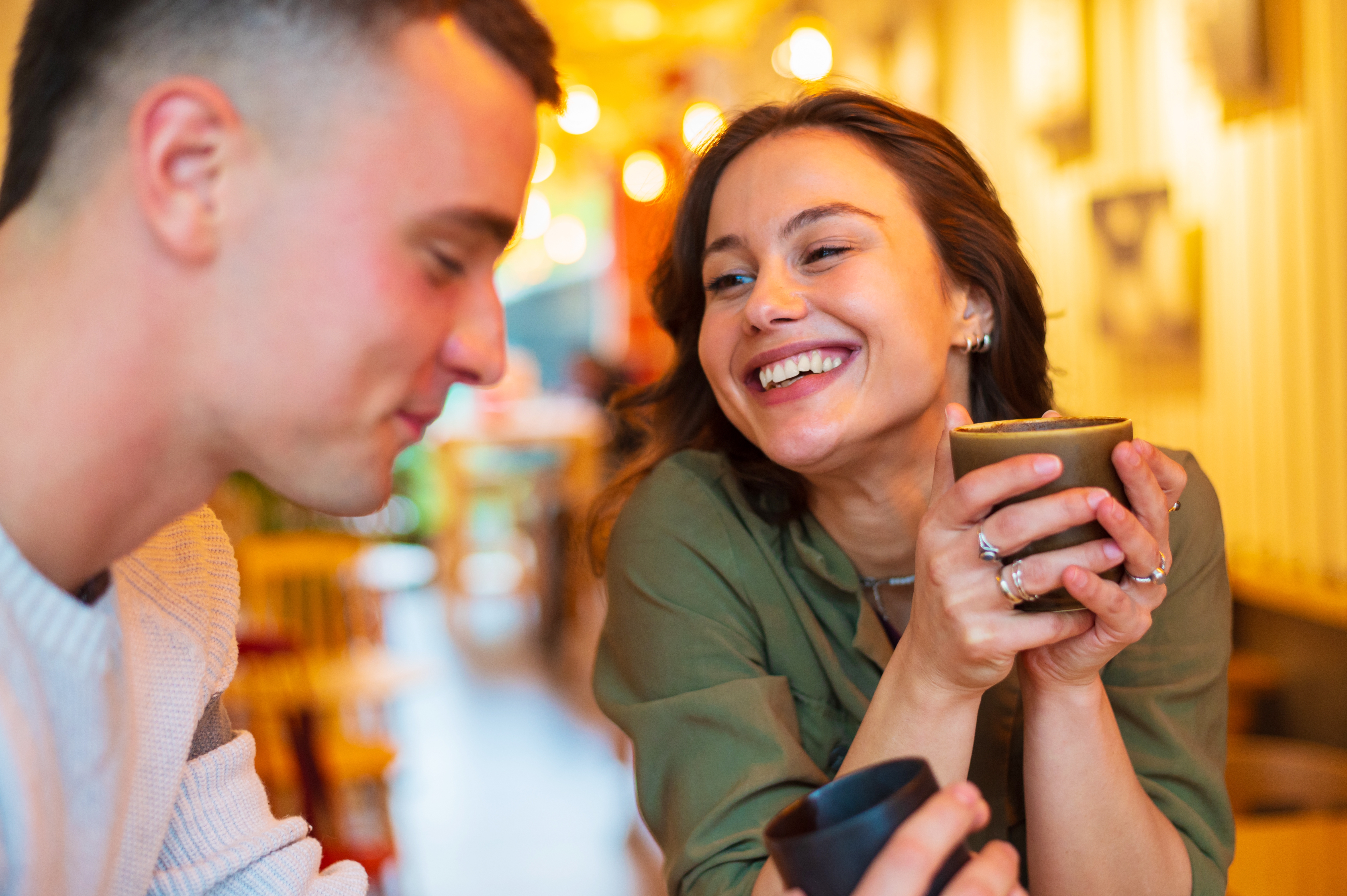 Et par nyter en koselig kaffedate, smilende og engasjert i samtalen, innendørs