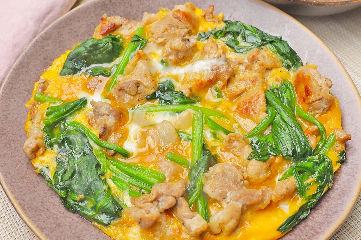 皿に盛られたオムレツ。緑野菜と肉がトッピングされ、美味しそうに仕上げられている。周囲に布と器が飾られている。