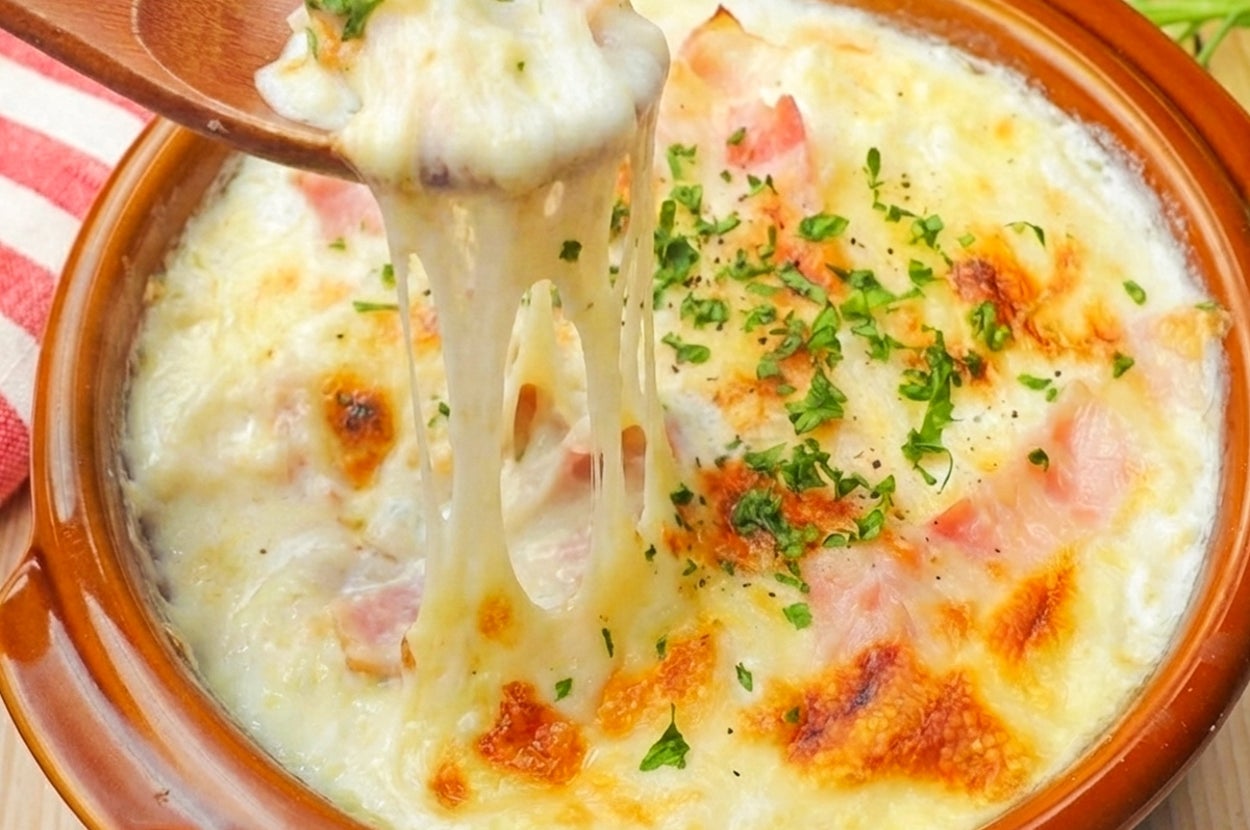 テーブルに置かれた焼きたてのグラタン。チーズがとろりとしていて、ハムやパセリがトッピングされている。