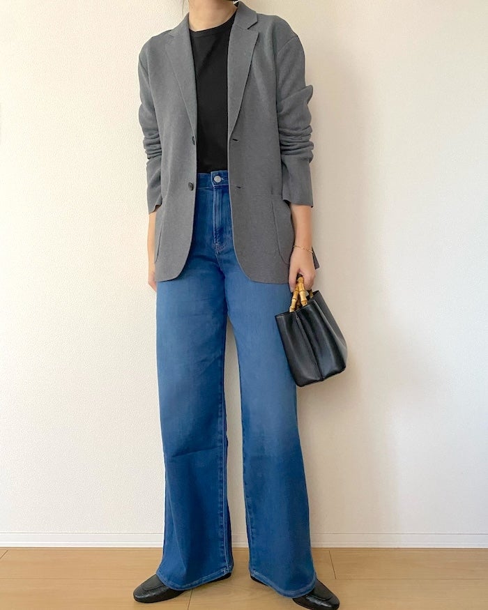 UNIQLO（ユニクロ）の「EZY ワイドストレート ジーンズ」女性がTシャツとブレザー、デニムジーンズ、黒い靴を着用し、黒いバッグを手に持って立っている。