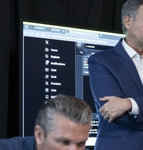 En gruppe menn, kledd i dress, samles rundt et stort bord med en bærbar datamaskin. De fremstår som engasjert i en seriøs diskusjon, med en delvis synlig skjerm