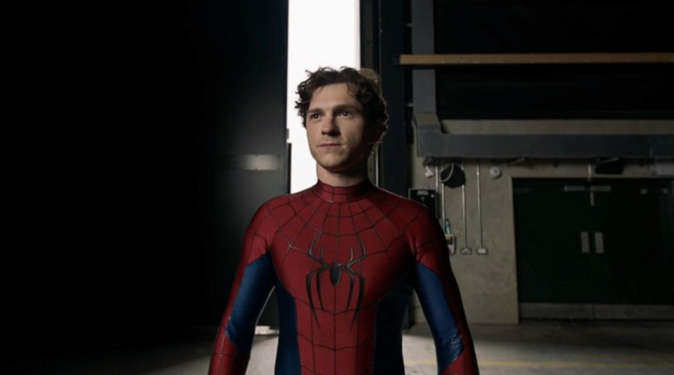 Orang berjas Spider-Man berdiri di ruangan remang-remang dekat pintu terbuka, tampak fokus