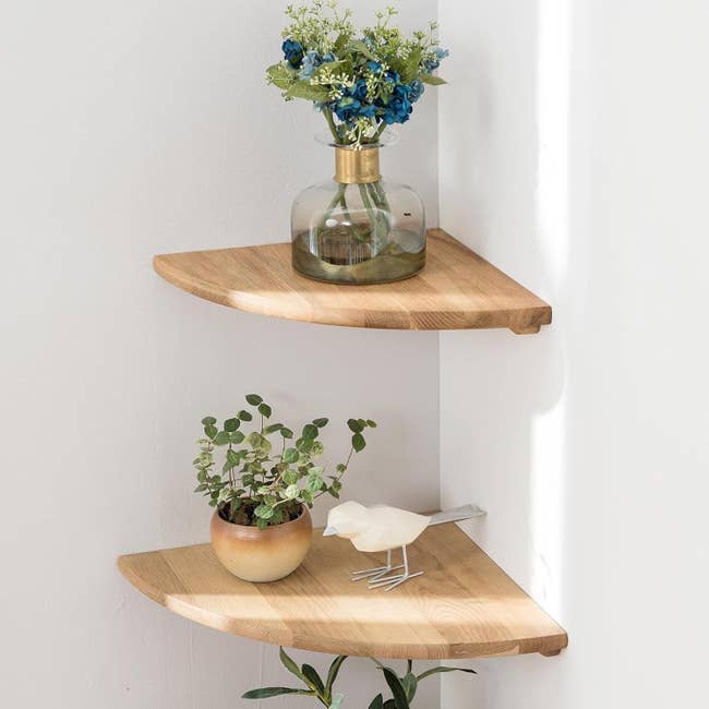 Corner woody  shelves with a vase of flowers connected  the apical  support  and a tiny  works  and vertebrate  figurine connected  the bottommost  shelf