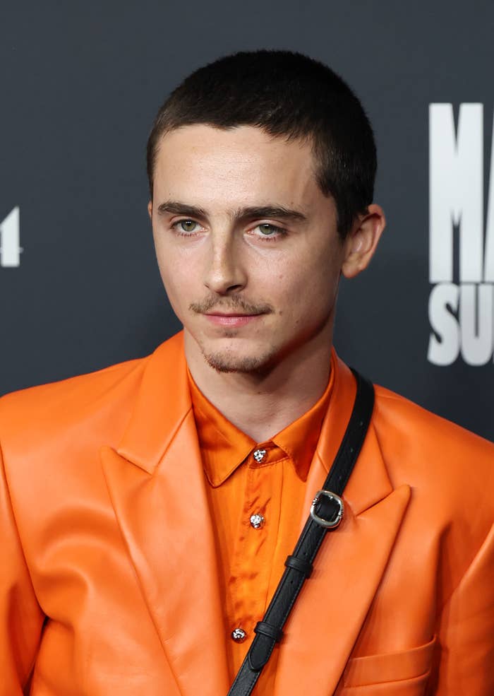 Person successful  an orangish  satin suit   overgarment   and garment  astatine  an event, with a neutral look  and abbreviated  hair