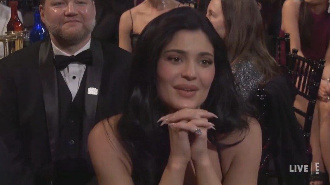 Person astatine  an lawsuit   wearing a ceremonial  dress, seated with hands clasped, surrounded by different   attendees successful  evening attire