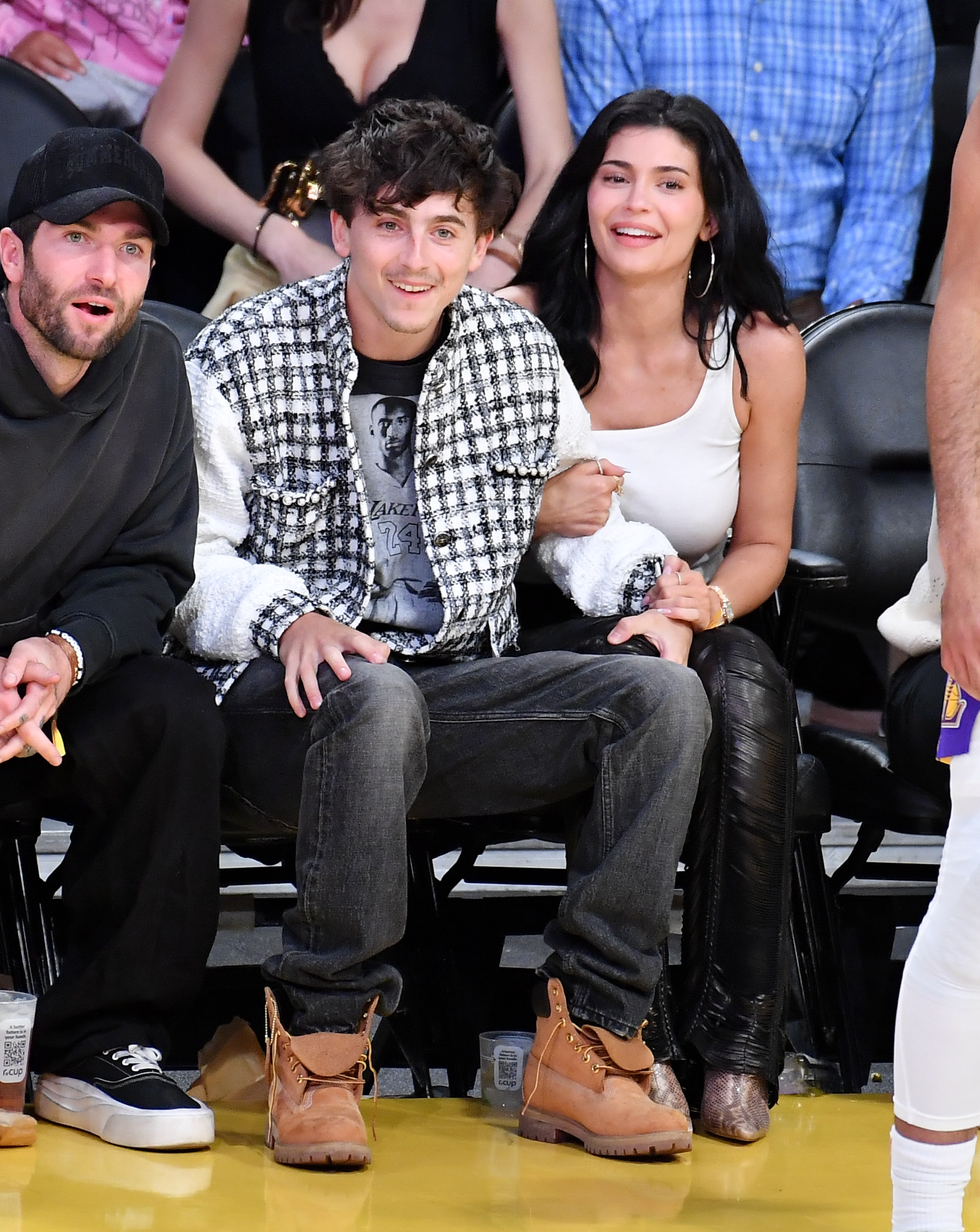A idiosyncratic   successful  a checkered overgarment   and jeans sits courtside astatine  a sports event, smiling alongside companions successful  casual attire