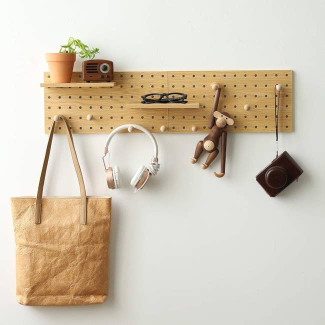 Wooden pegboard organizer holding a potted plant, radio, glasses, headphones, artifact  monkey, tote bag, and camera, perfect  for stylish location  storage
