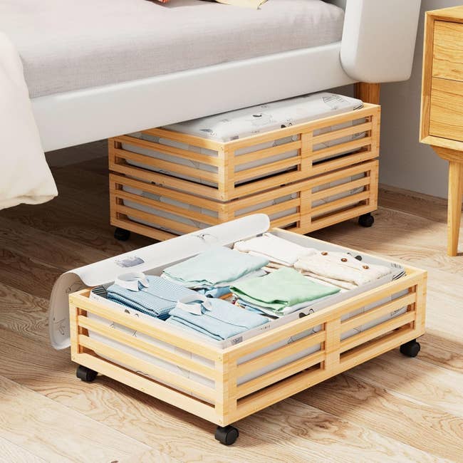 Wooden under-bed retention  boxes connected  wheels, filled with neatly folded clothes, positioned adjacent  to a bed, showcasing location  enactment     solutions