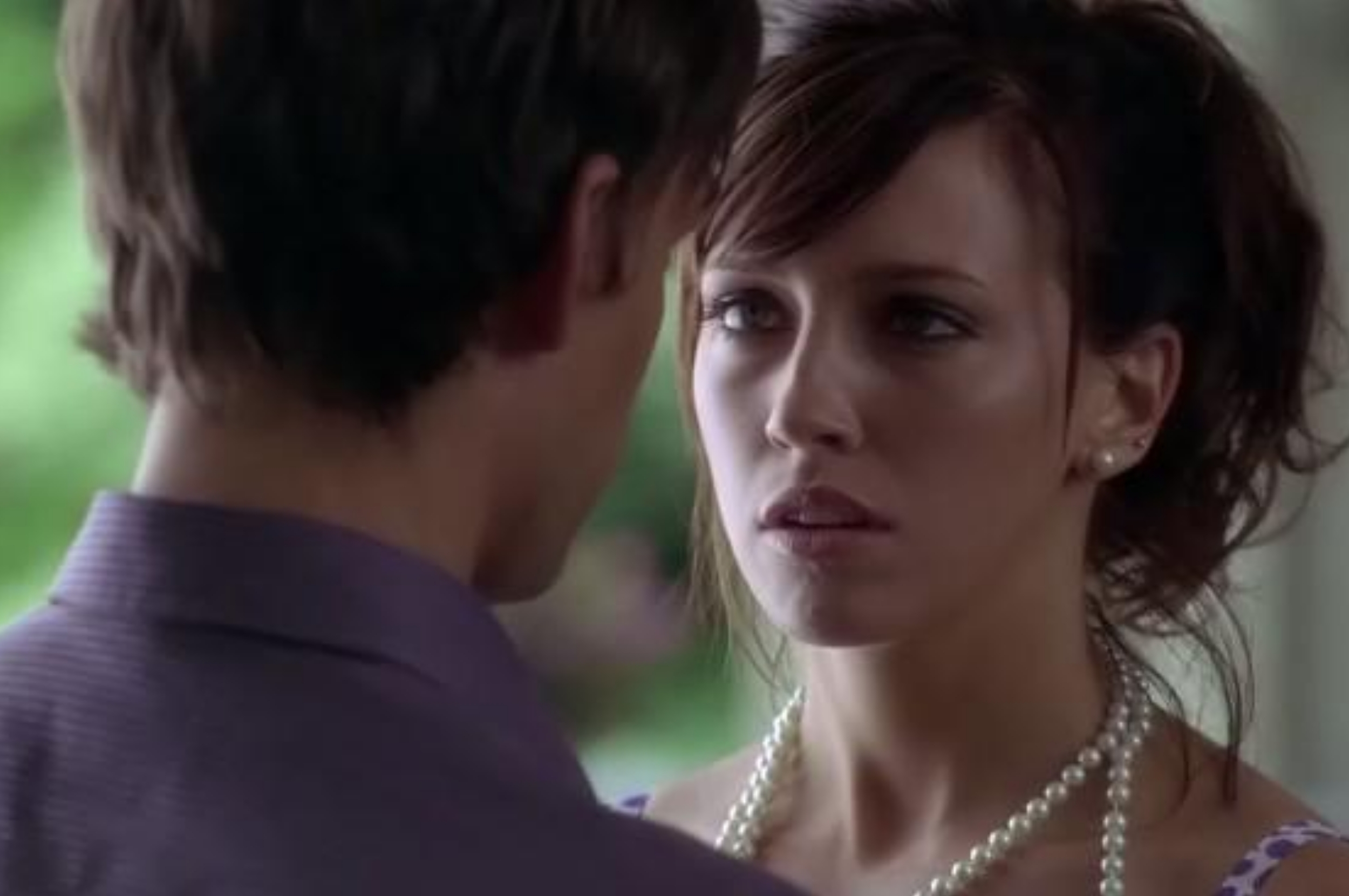 Two people facing each other closely, showing intense emotion. The woman wears a pearl necklace and the man is seen from behind
