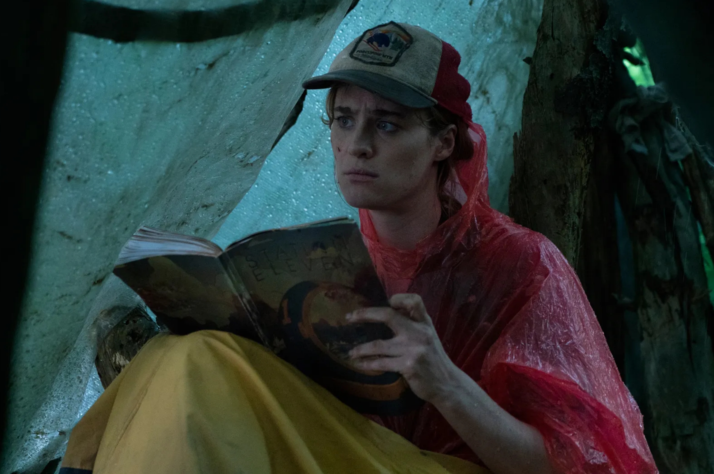 Person in a red poncho and cap is intensely reading a comic book. They are seated in a sheltered outdoor area