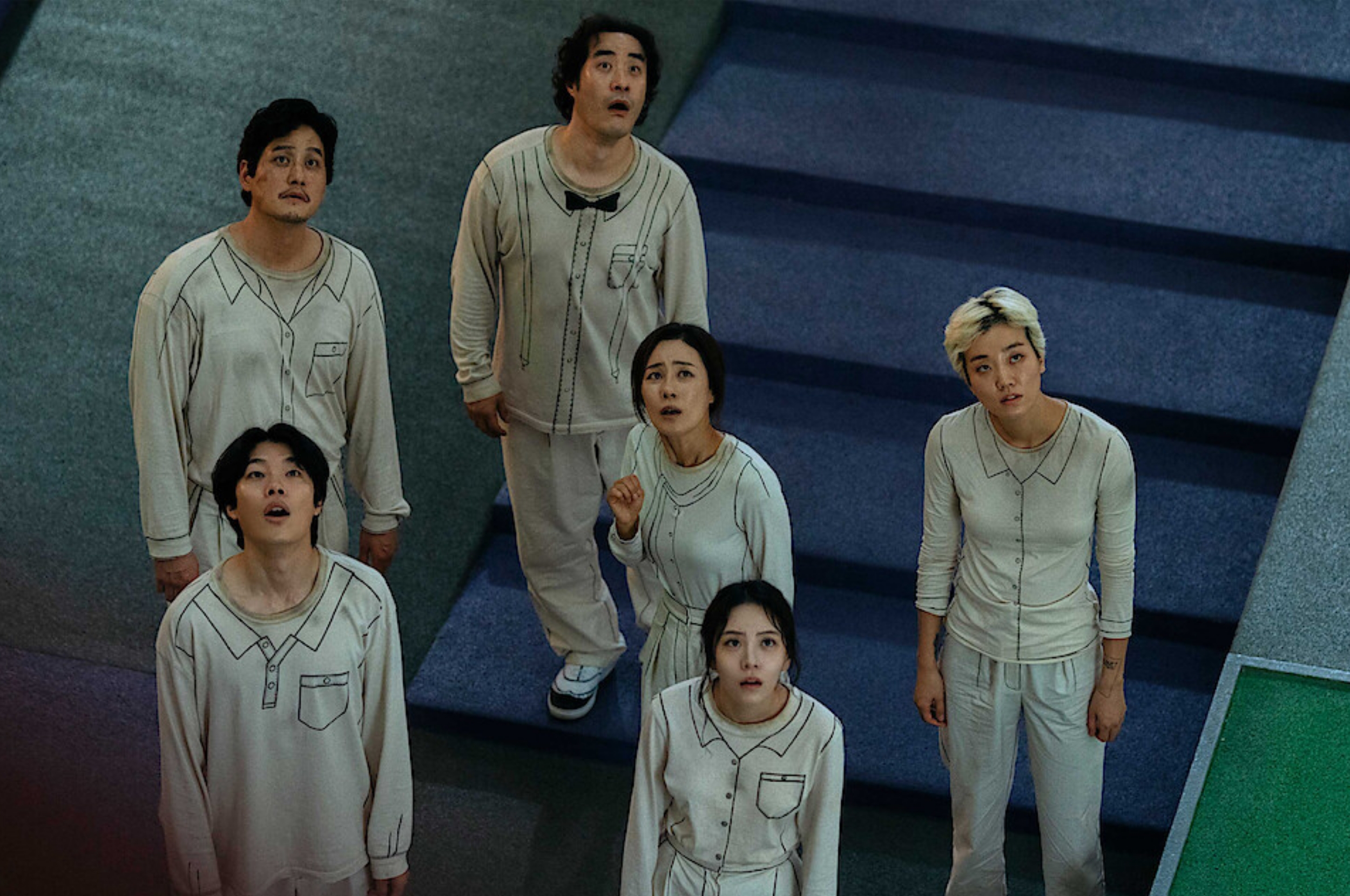 Six people in casual, matching outfits look upward with expressions of surprise or concern