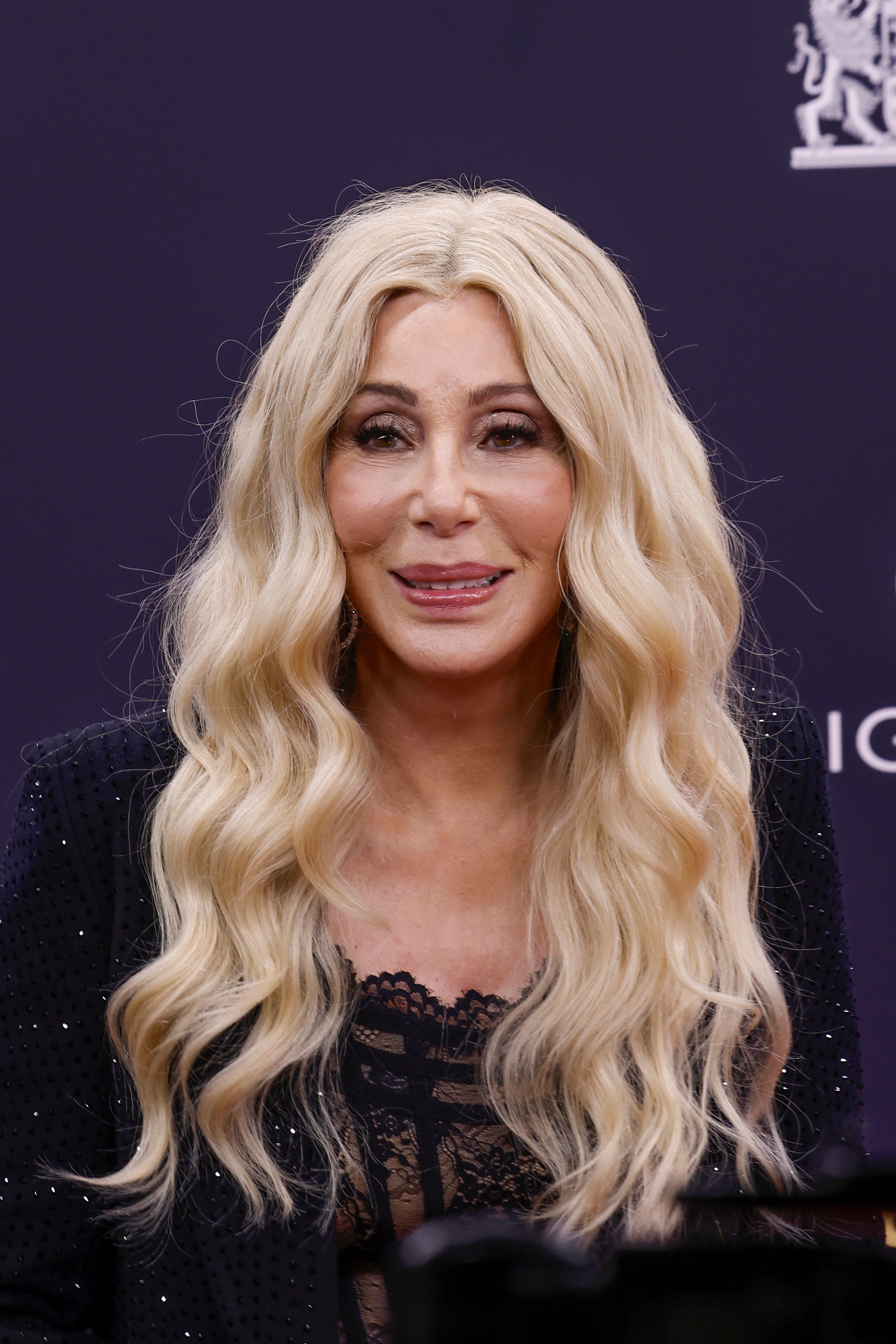 Person with long wavy hair wearing a lace-accented outfit at a formal event
