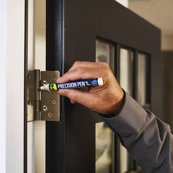 Person applying lubricant to a doorway hinge with a precision pen