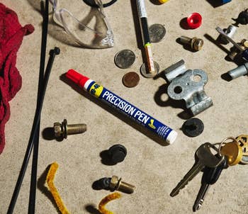 Precision Pen instrumentality amongst assorted keys, bolts, and tiny hardware items connected a workbench, with a reddish cloth nearby