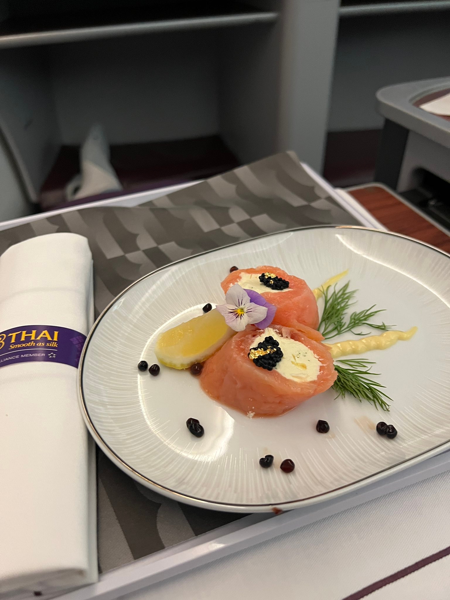 En tallerken med røkt lakseruller fylt med kremost, garnert med kaviar, sitronskiver, dill og spiselige blomster på en elegant borddekking