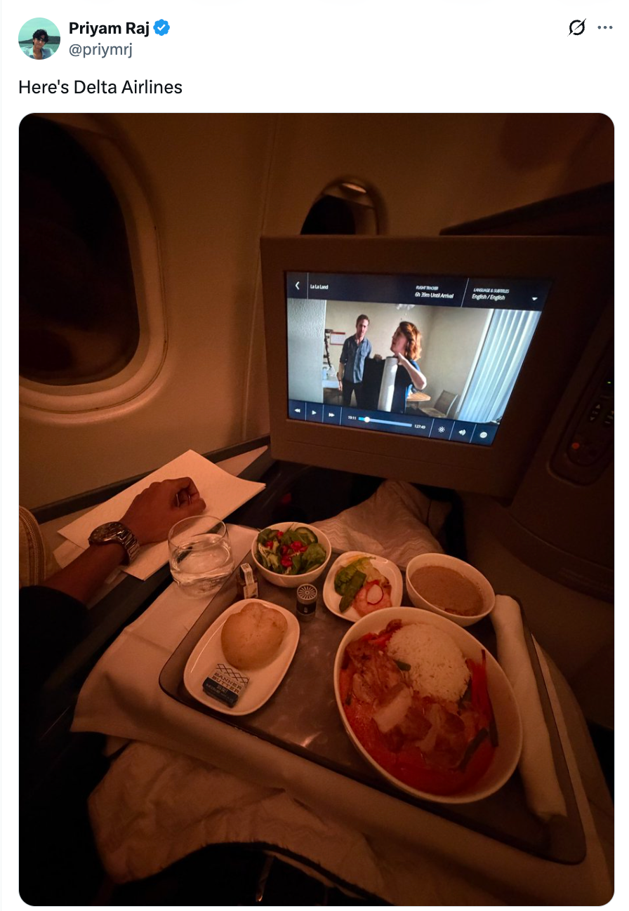 Flymåltid på et brett med salat, brød, ris og karri; skjerm som viser en filmscene i en svakt opplyst Delta Airlines-hytte