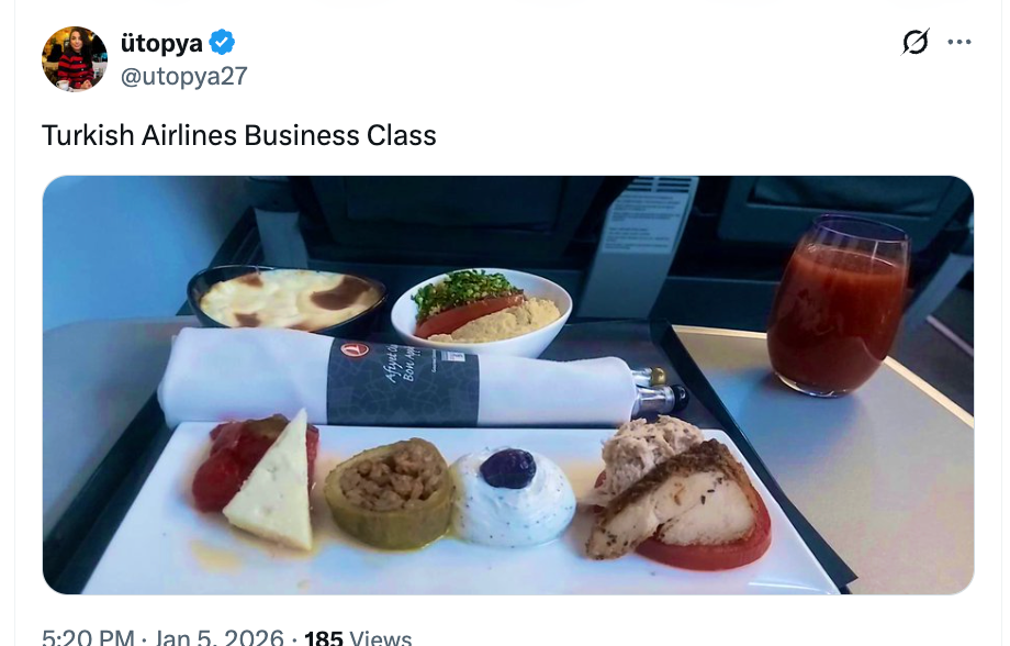 Brett med forskjellige tyrkiske forretter og desserter på et brettbord for flyselskaper, inkludert en innpakket serviett og et glass tomatjuice