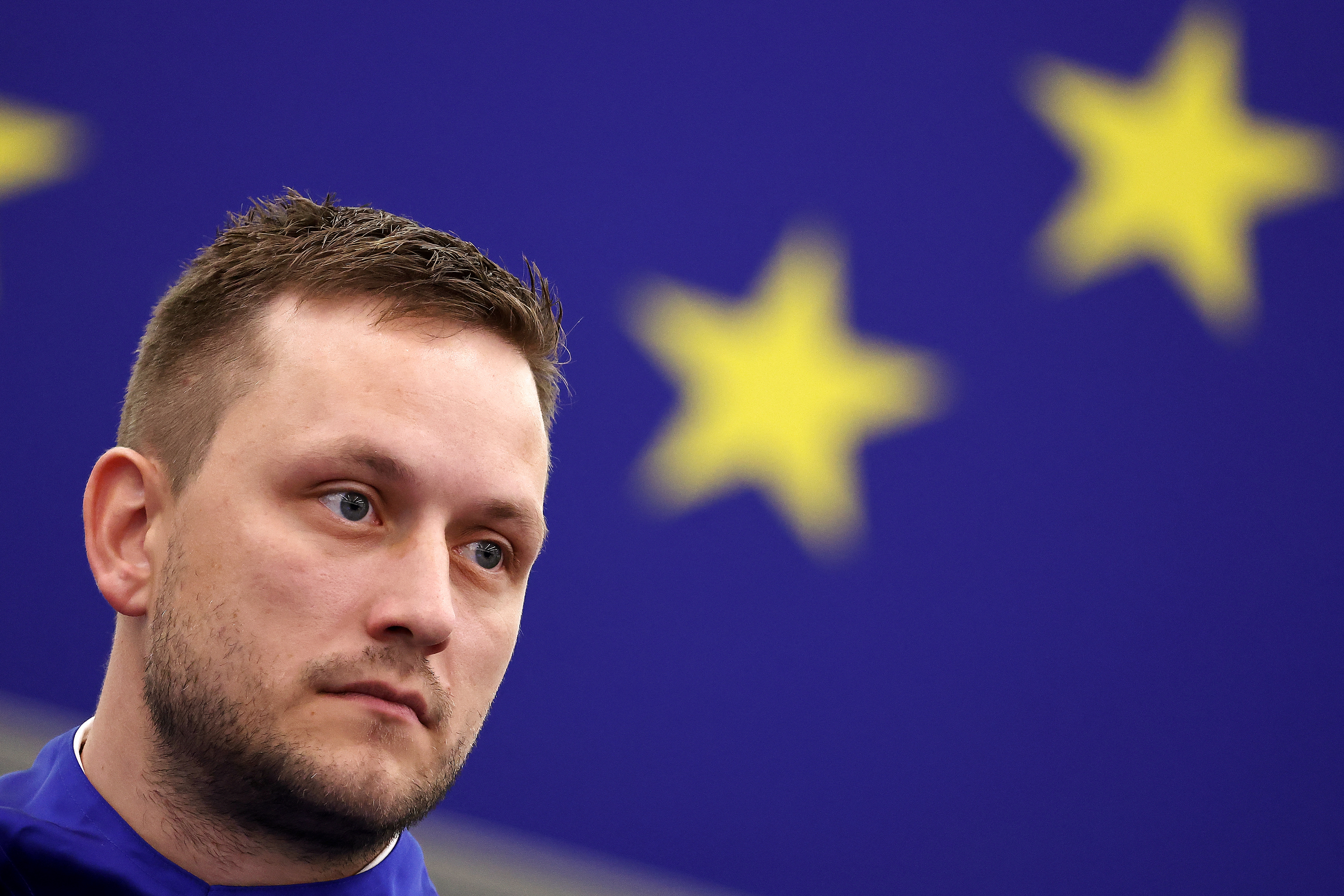 En person står foran et bakteppe med store gule stjerner, vanligvis assosiert med EU-flagget