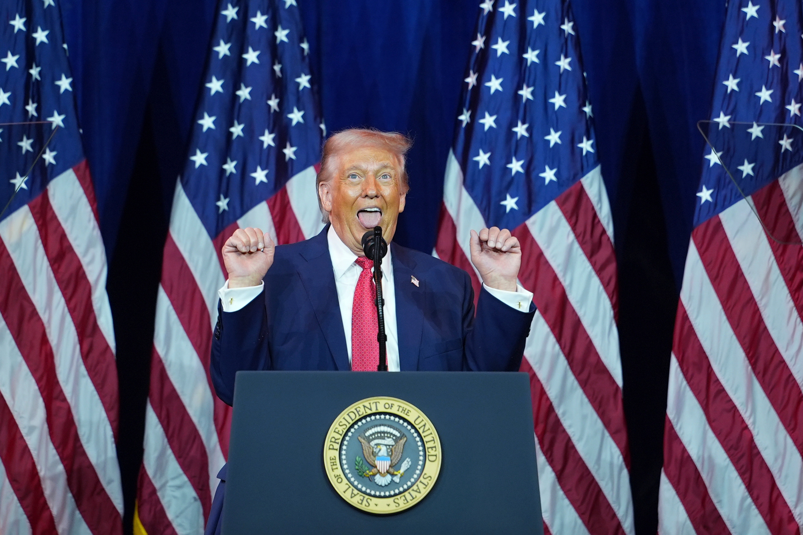 En person som snakker entusiastisk ved et podium med flere amerikanske flagg i bakgrunnen