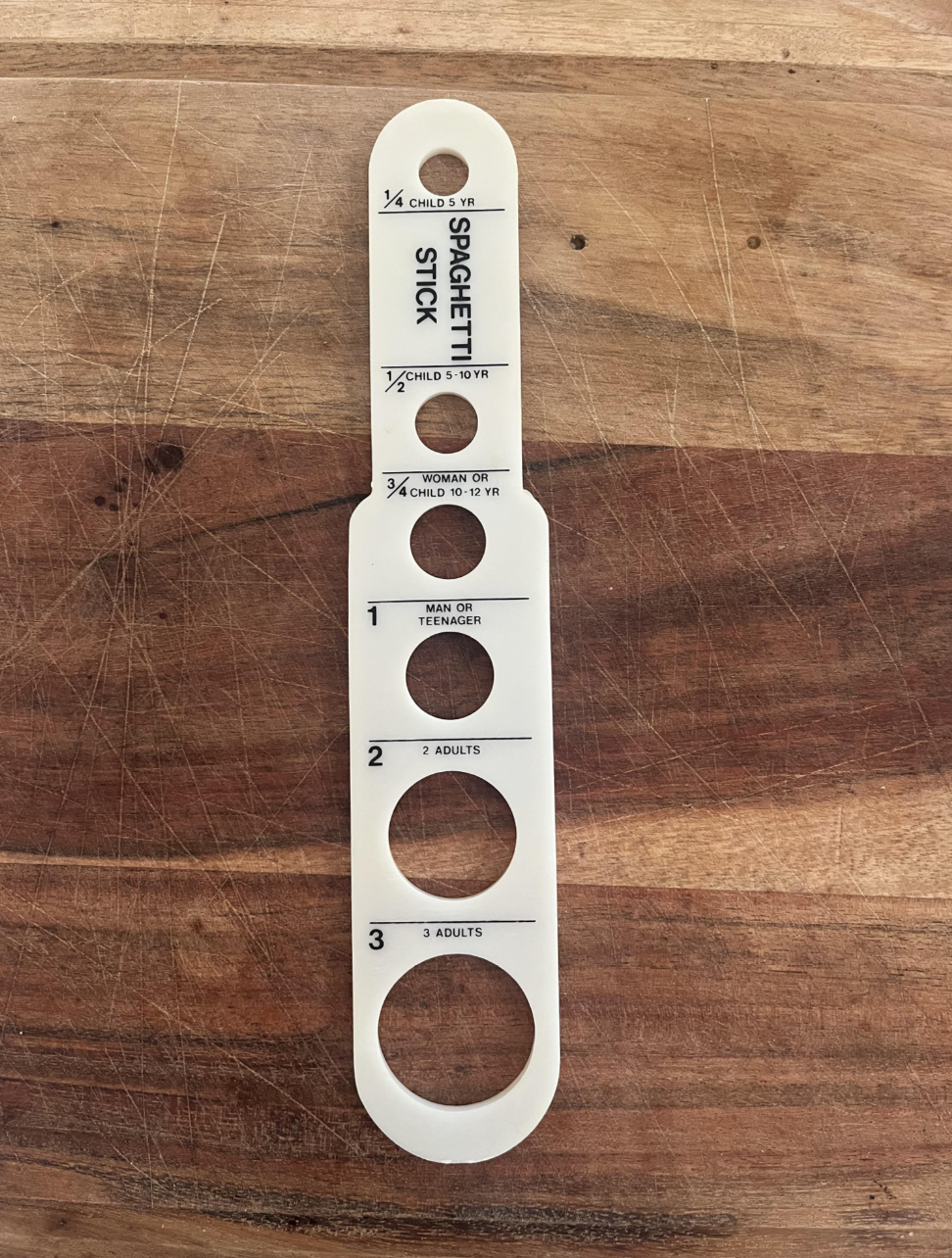 Spaghetti portion measurer on a wooden surface, labeled for child, adult, and family servings by weight and age guide