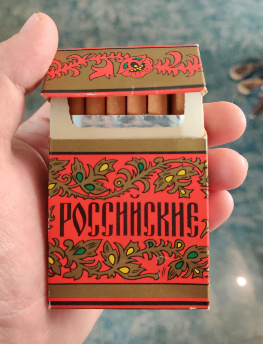 Hand holding an ornate cigarette pack with Cyrillic text and floral design