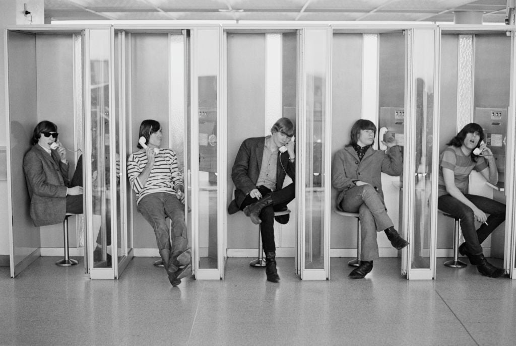 Five radical   utilizing rotary payphones successful  abstracted  telephone  booths, each   seated and engaged successful  conversation