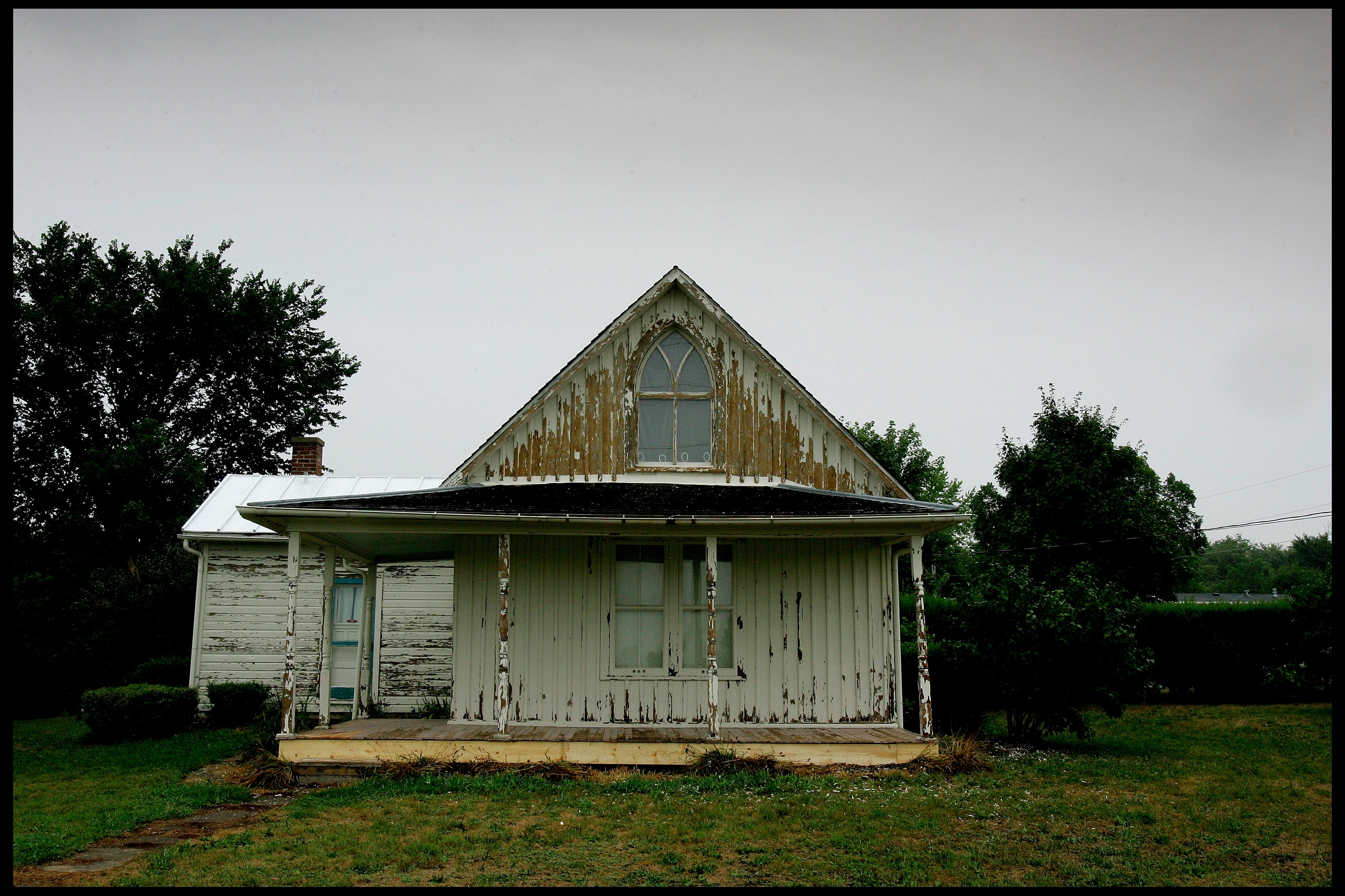 An old, weathered achromatic  location   with a triangular extortion   and peeling overgarment   stands amid greenery connected  a cloudy day