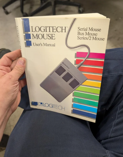 A person is holding a Logitech Mouse User's Manual featuring an image of a wired mouse and colorful stripes on the cover