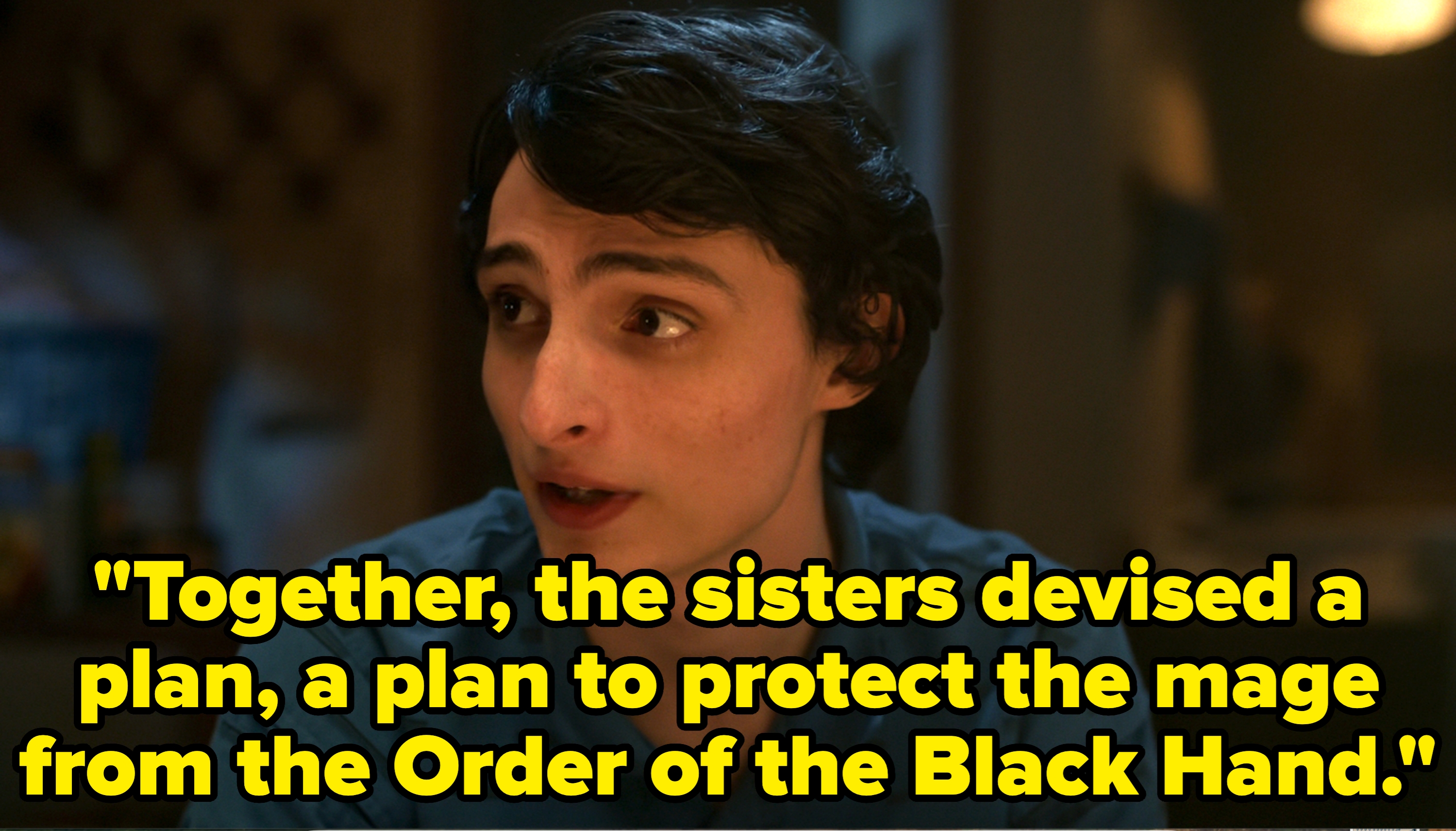 Person with short, dark hair and patterned shirt looks to the side, seemingly engaged in conversation. Background is softly blurred