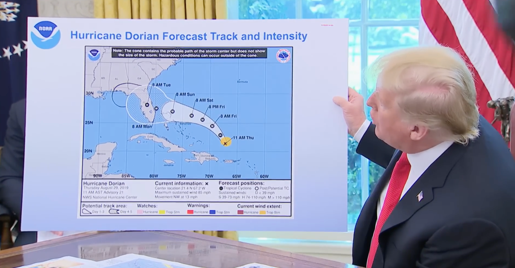 Person i dress holder et kart som viser orkanen Dorians anslåtte bane og intensitet, med ekstra håndtegnet linje som forlenger banen