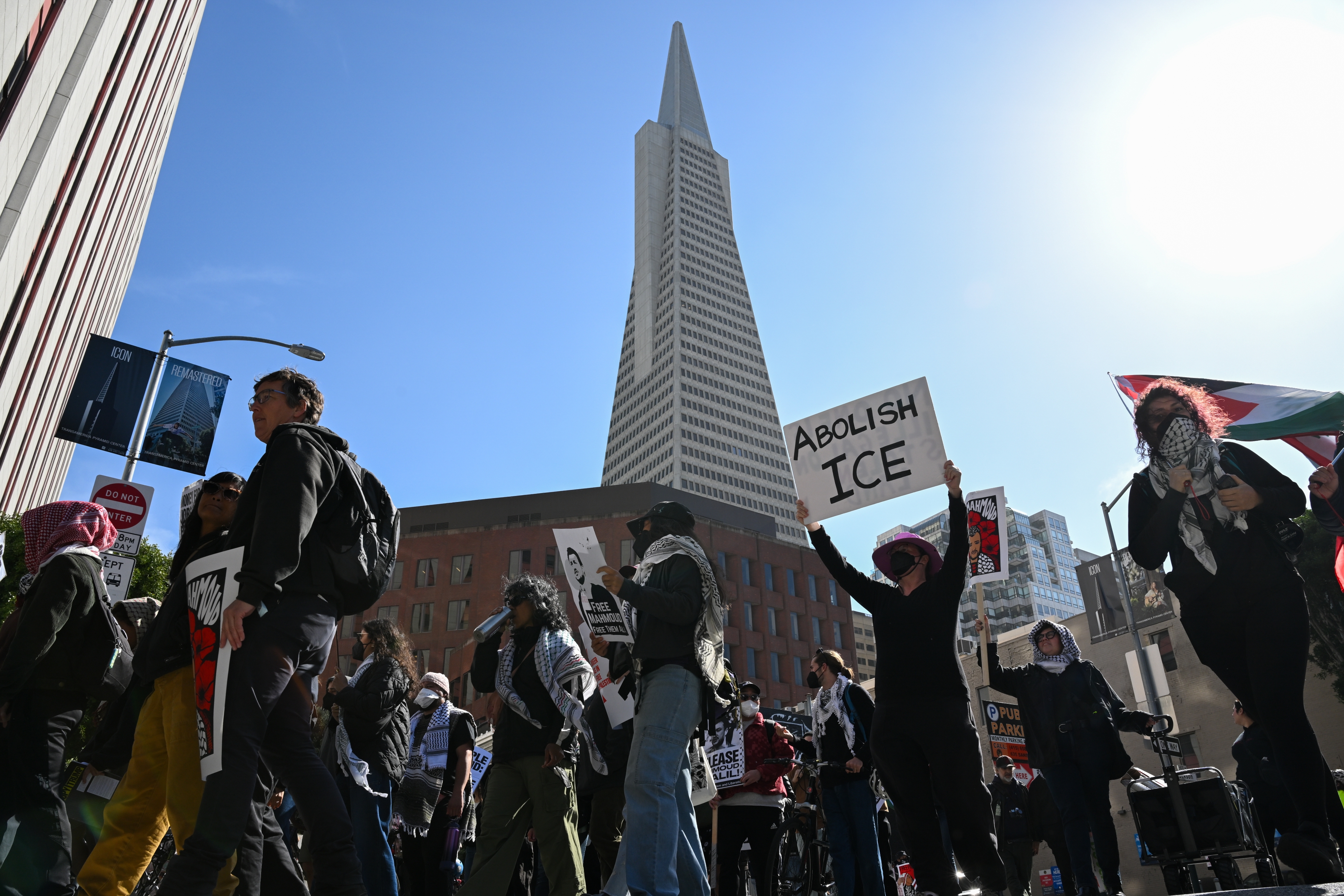 Demonstranter marsjerer med skilt mot ICE under en høy bygning, og viser solidaritet og talsmann for innvandrerrettigheter