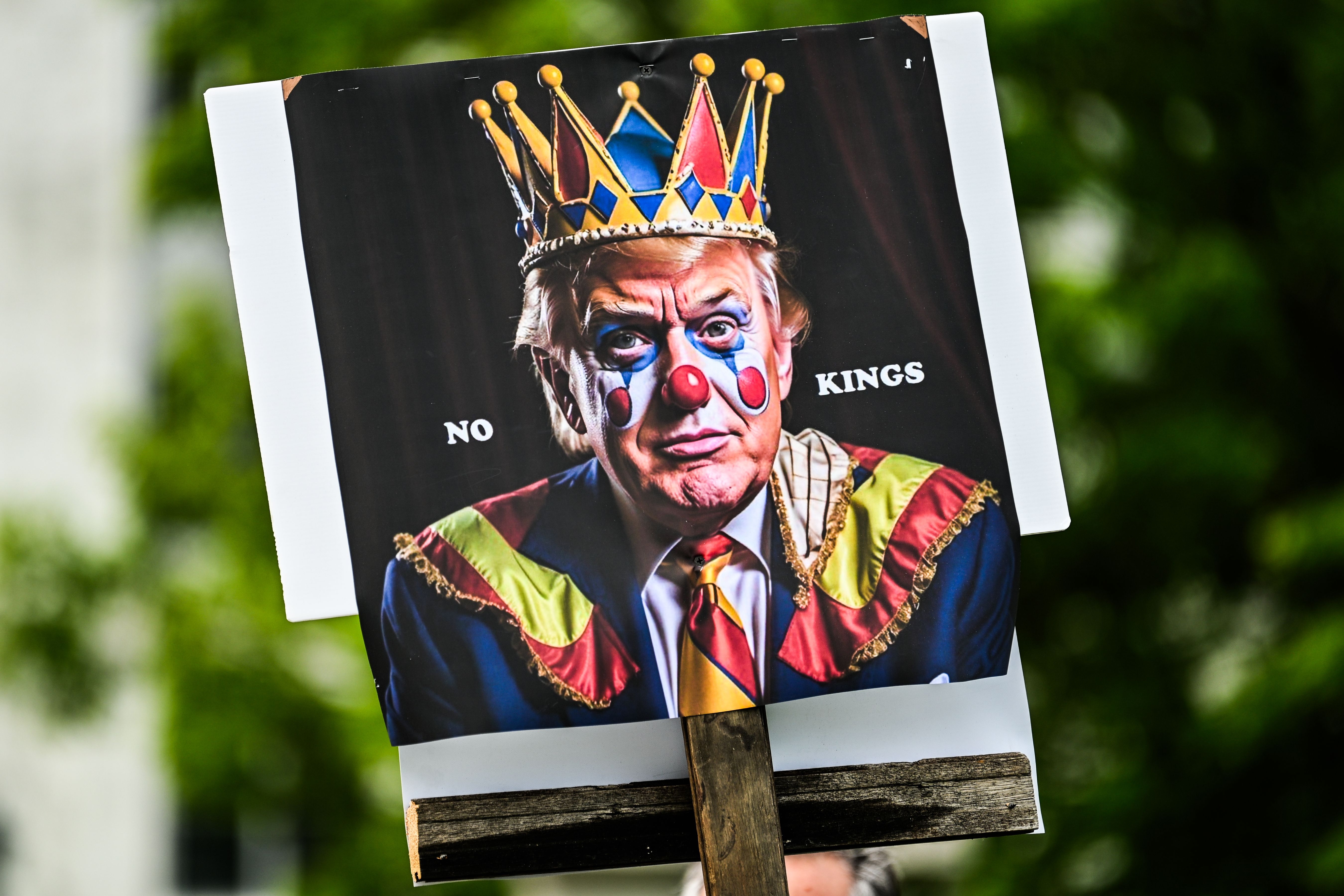 Protestskilt som viser en person med klovnesminke og krone, merket «Ingen konger»; som indikerer en kritikk av autoritet eller lederskap