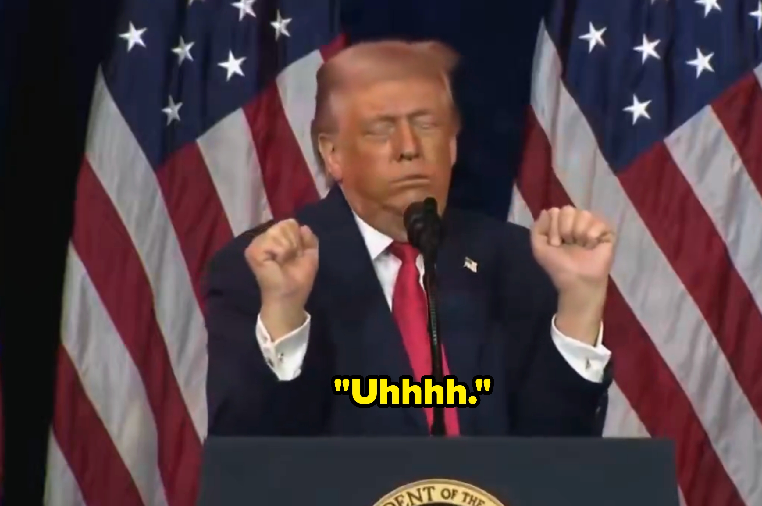 En person som står med lukkede øyne og hevede never, foran amerikanske flagg, og snakker inn i en mikrofon med ordet 