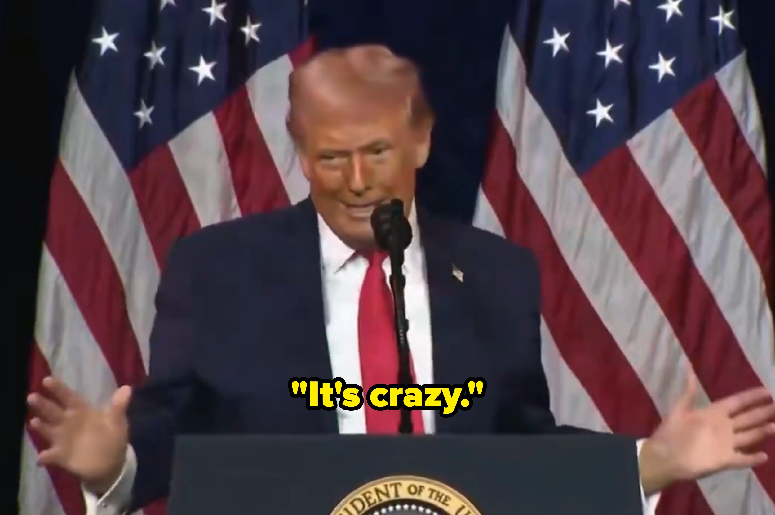 Person som snakker på et podium med amerikanske flagg i bakgrunnen, gestikulerer med hendene. Tekstoverlegget lyder: 