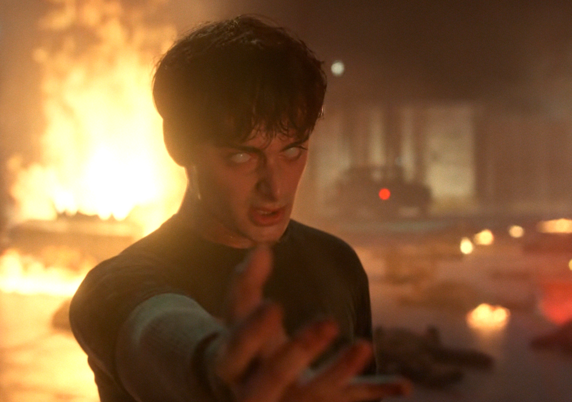 A person with an intense expression reaches forward amid flames and debris, creating a dramatic scene