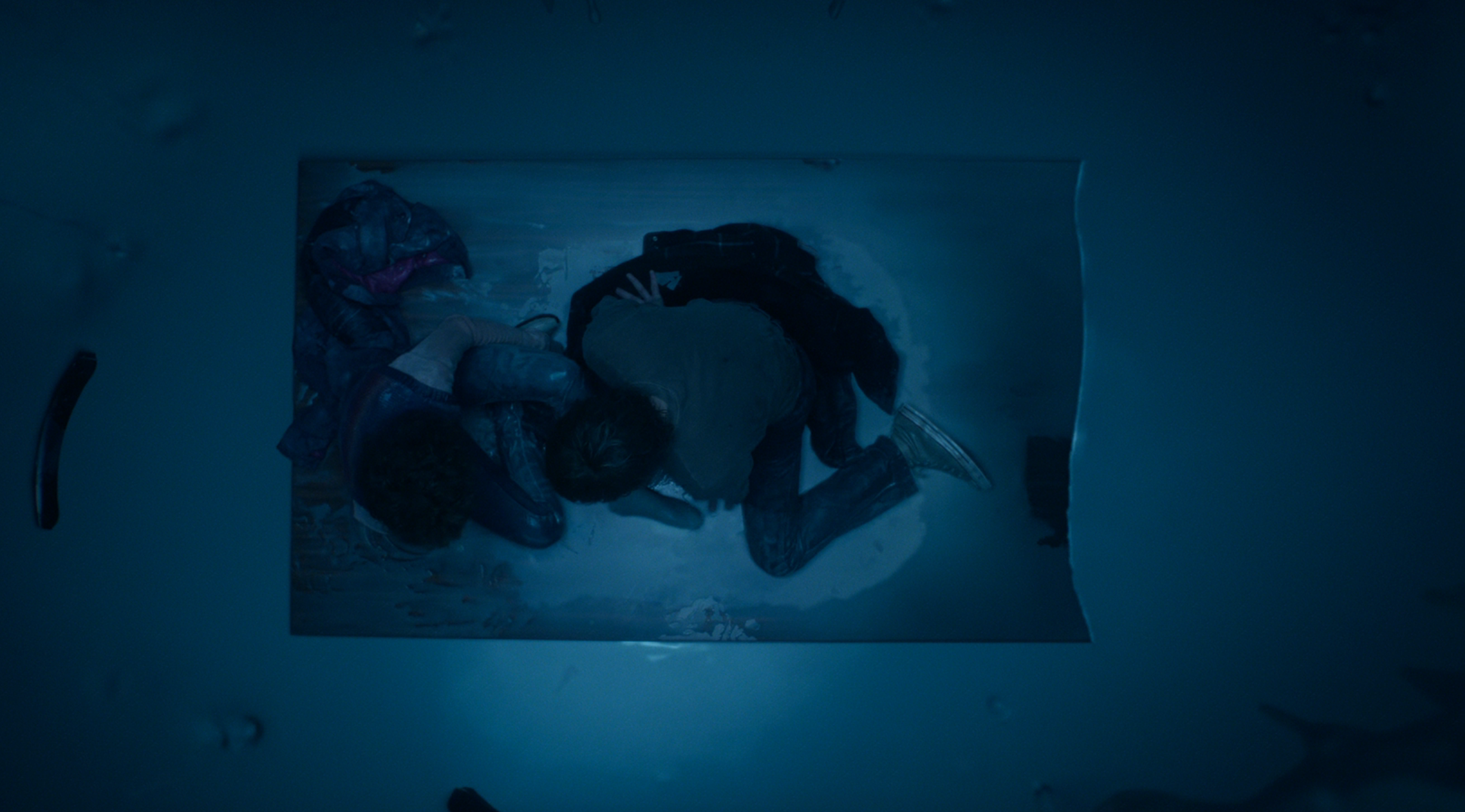 Two people lying side by side on a floating door in the ocean, viewed from above, simulating a famous movie scene