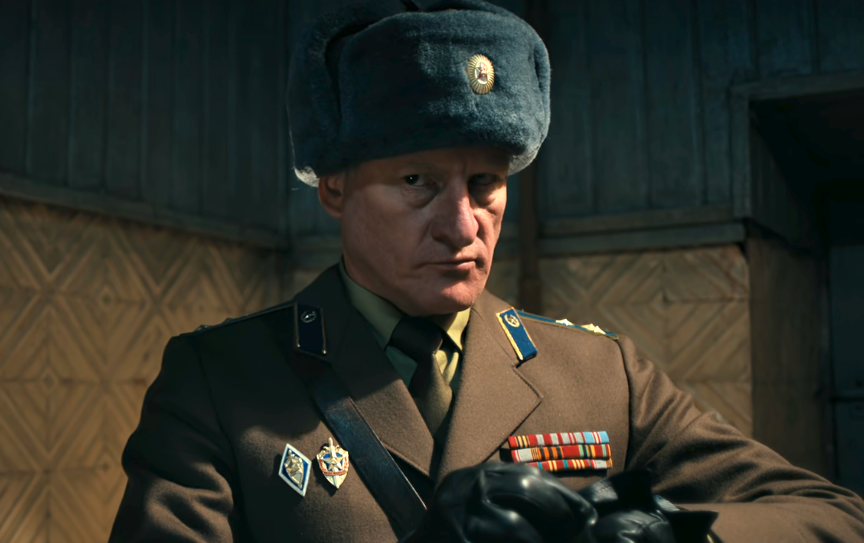 Person in a military uniform and fur hat, looking serious, adjusting gloves
