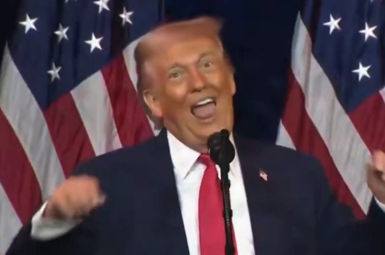 Person animatedly speaking at a podium with U.S. flags in the background