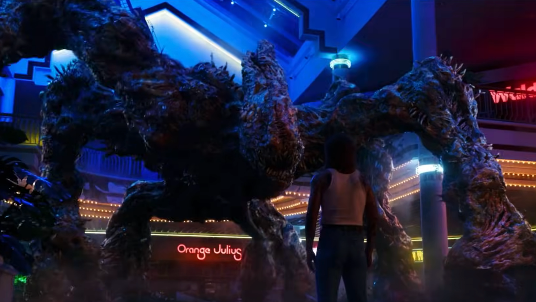 A person stands in front of a large, menacing, tree-like creature in a neon-lit mall setting
