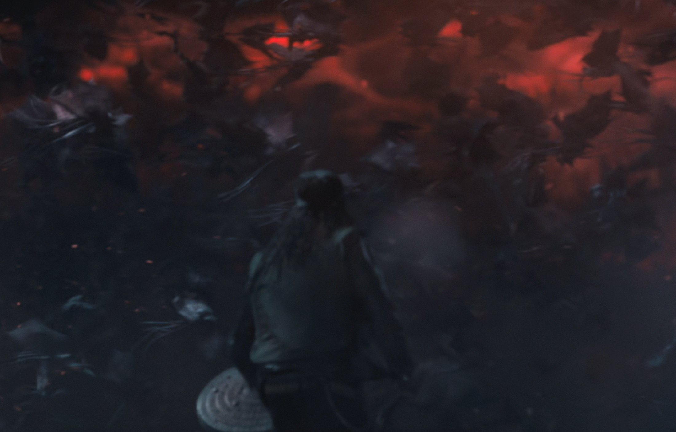 A figure in a cloak and hat stands facing a swirling storm of bats illuminated by a glowing red sky