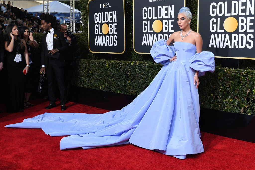 Person in an elegant gown with voluminous sleeves and long train on a red carpet at the Golden Globe Awards