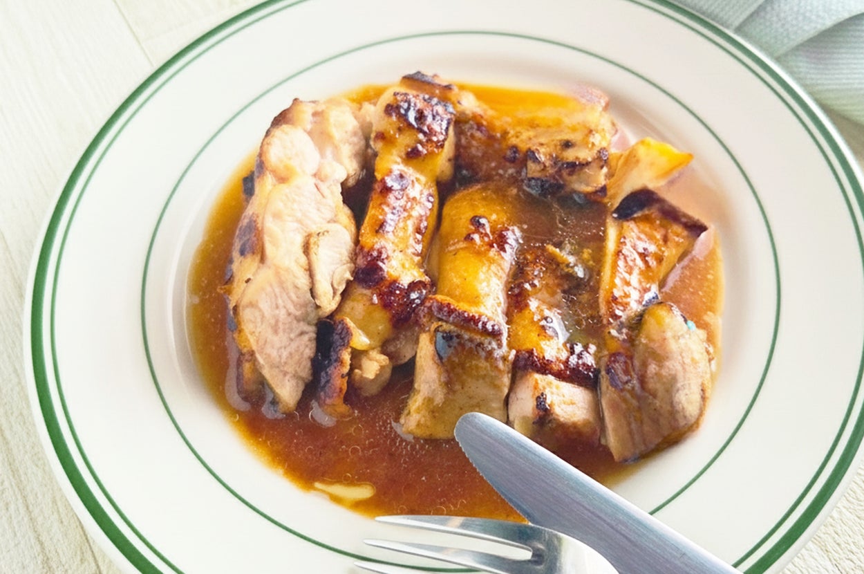 皿に盛られたグリルチキンがソースに載っており、横にフォークとナイフが添えられています。