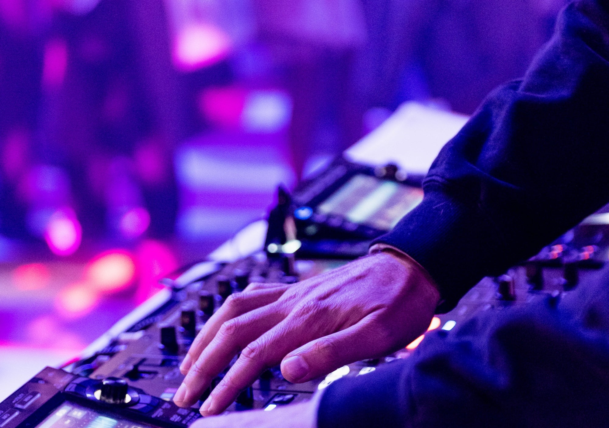 DJ performing at an event, hands on a mixing console, surrounded by an energetic crowd